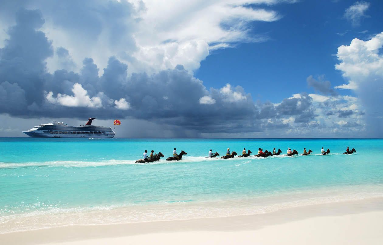 The group of tourists riding horses along the beach on Half Moon Cay  The Bahamas  