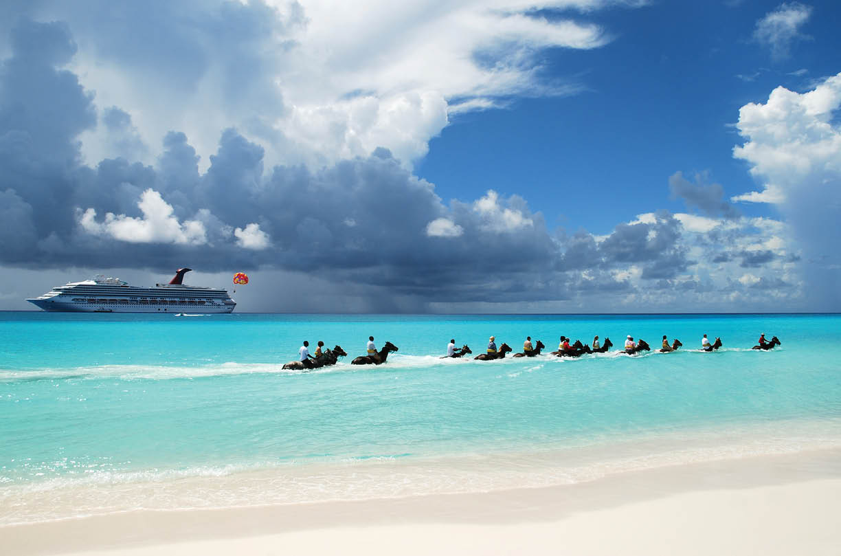 The group of tourists riding horses along the beach on Half Moon Cay  The Bahamas  
