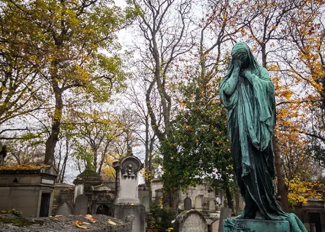 A weathered statue stands among the tombstones in Pére Lachaise Cemetery