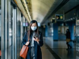 Asian woman with protective face mask using smartphone while walking on the subway platform
