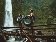 Travel Hacks That Will Help You Enjoy The World On A Budget couple walking on a wooden bridge to a remote waterfall