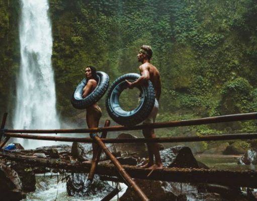 Travel Hacks That Will Help You Enjoy The World On A Budget couple walking on a wooden bridge to a remote waterfall