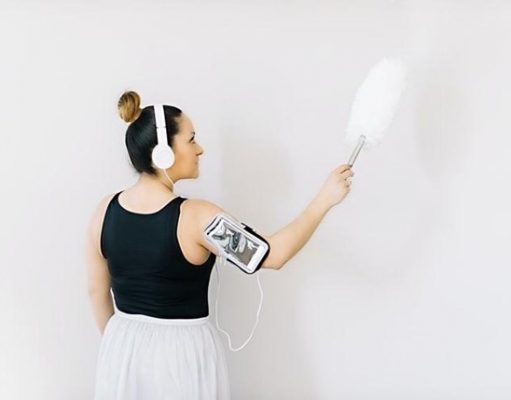 10 Easy Home Cleaning Preparations You Need to Do Before Your Vacation girl dusting a wall while listening to music