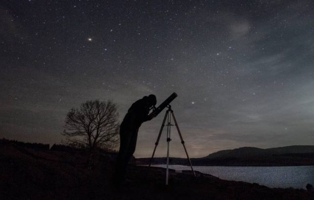 person llooking at the night sky through a telescope