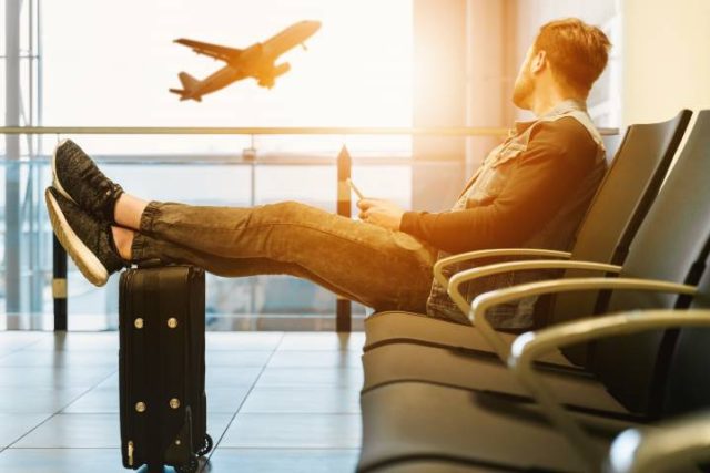 man sitting an airport watching a plane take off