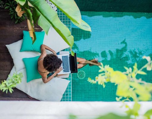 Workations, The Future? Or Just Another Travel Trend woman working on a laptop while sitting at a pool