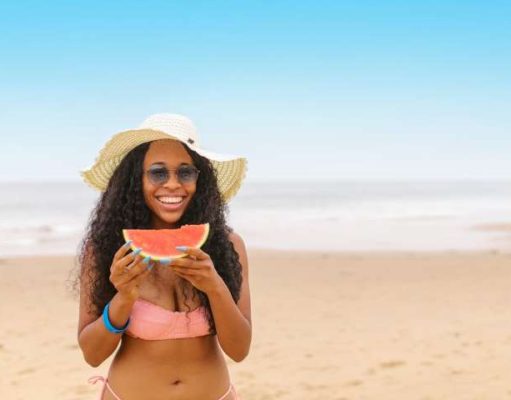 How to Maintain Your Fitness Diet on Summer Vacation girl on beach eating watermelon