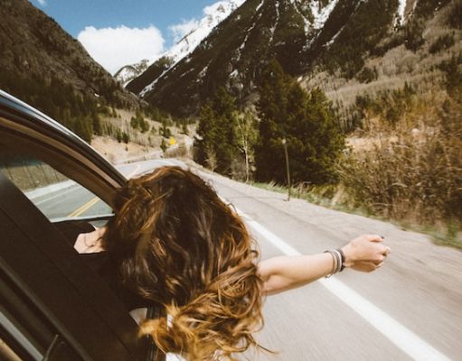 6 Things You Should Bring On Your Next Trip girl hanging out car window while traveling down the highway