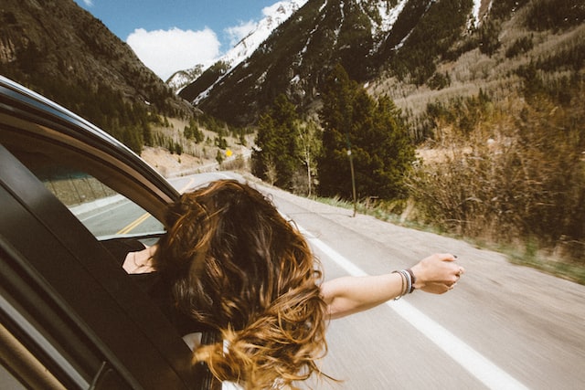 girl hanging out car window while traveling down the highway