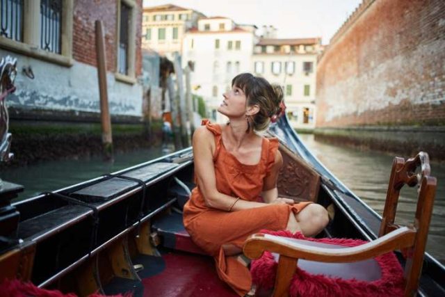 A young woman rides a gondola through Venice