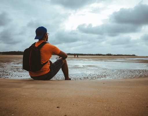 Tips to Make the Most of Your Beach Vacation This Fall Man in Orange Shirt with Backpack Sitting on Beach Sand