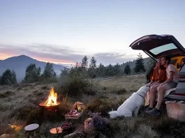 couple sitting on the back of their car at a camp fire