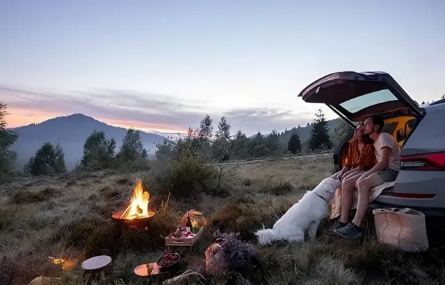 couple sitting on the back of their car at a camp fire