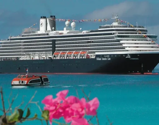 Fresh Puerto Rican Tostones and Stone Crab Highlight New Caribbean Menu on Holland America Line A large multi-deck cruise ship with the label "Holland America Line" anchored in clear turquoise waters. In the foreground, there's a smaller orange and white boat floating on the water. Vibrant pink flowers are visible in the lower right corner, providing a contrast to the vast blue sea backdrop. The sky above is clear and blue.