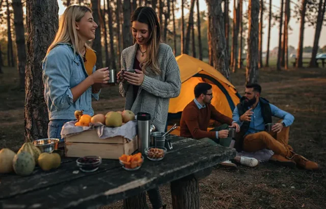 Young women enjoying hot drink at the forest during autumn weekend