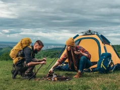 How to Prepare for Your First Camping Trip Abroad Couple of campers lighting a fire while setting up the camp tent