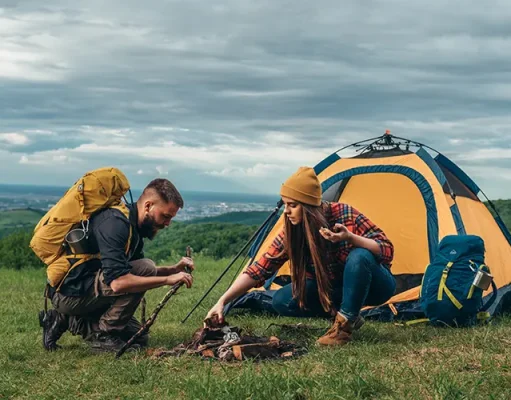 How to Prepare for Your First Camping Trip Abroad Couple of campers lighting a fire while setting up the camp tent