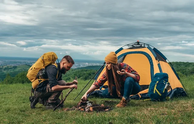 Couple of campers lighting a fire while setting up the camp tent