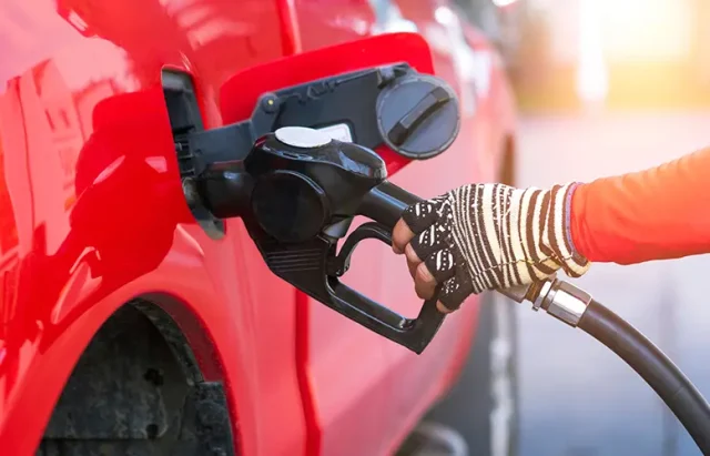 worker hand holding nozzle for filling diesel fuel into red pick up car at refuel station