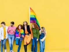 Greater Miami LGBTQ+ Chamber Of Commerce Launches Pink Flamingo Hospitality Initiative Young group of people leaning on yellow background celebrating together LGBTQI gay pride festival day. LGBT young friends having fun together outdoors.
