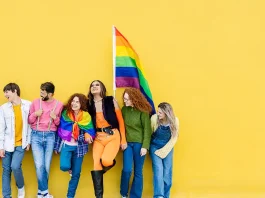 Young group of people leaning on yellow background celebrating together LGBTQI gay pride festival day. LGBT young friends having fun together outdoors.