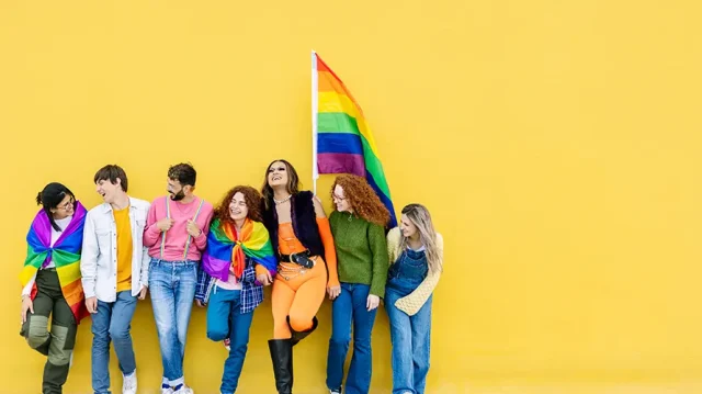 Young group of people leaning on yellow background celebrating together LGBTQI gay pride festival day. LGBT young friends having fun together outdoors.
