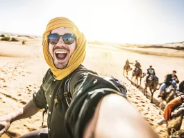 Happy tourist having fun enjoying group camel ride tour in the desert