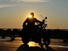 Solo Motorcycle Travel Safety: Tips for Riding Alone silhouette of a man on a motorcycle on the road, behind him the setting sun, warm, yellow tones
