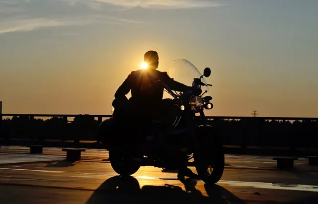 silhouette of a man on a motorcycle on the road, behind him the setting sun, warm, yellow tones