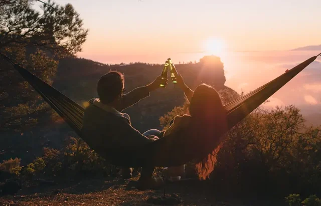 beautiful couple seated in a hammock toasting with a cloudscape sunset