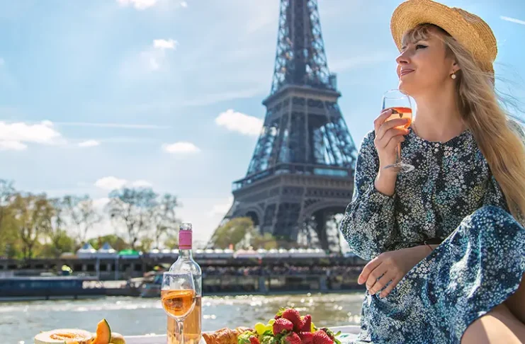 A woman near the Eiffel Tower drinks wine