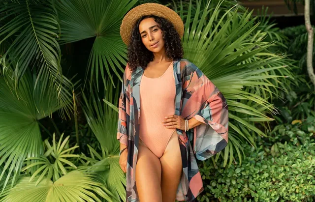 woman in straw hat and summer stylish outfit posing in tropical garden