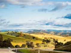 Capturing Australia’s Beauty: Creating Photogenic Road Trip Itineraries Open empty road surrounded by green hills, fields and farms in Australia. Road trip background