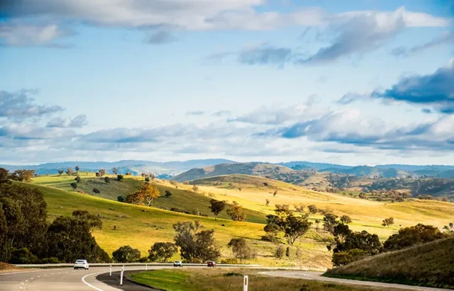 Open empty road surrounded by green hills, fields and farms in Australia. Road trip background