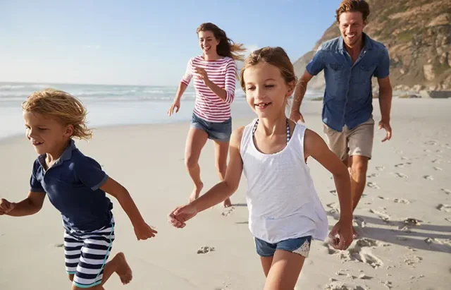 Parents Running Along Beach With Children On Spring Break Vacation