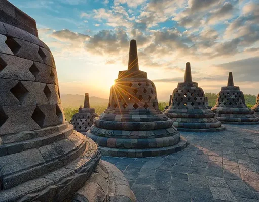 Adventure Life Offers New Land Tours in Indonesia, Mexico, Canada and More A stunning sunrise view at the ancient Buddhist temple of Borobudur in Java, Indonesia. The photo captures the silhouette of multiple stupas, each adorned with intricately carved stone lattices, against the golden light of the sun peeking through the main stupa. The surrounding landscape of lush mountains under a sky scattered with soft clouds adds to the tranquil and historic ambiance.