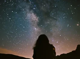 The Milky Way stretches across the firmament, a swath of cosmic dust and countless stars offering a breathtaking view. The silhouette of the person adds a sense of scale and wonder, as they gaze up at the vast universe. It's a reminder of the infinite beauty that lies beyond our own planet.