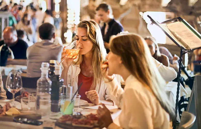 A woman drinking wine and eating with her friend in a restaurant