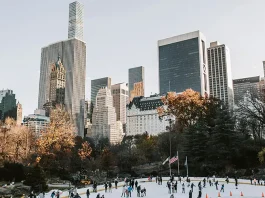 People ice skating in the park with buildings in the back