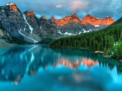 Exploring Canada’s Scenic Routes During Your Cross-province Move A stunning view of a tranquil lake surrounded by lush pine trees and snow-capped mountains during sunset, capturing the beauty of exploring Canada's scenic routes.