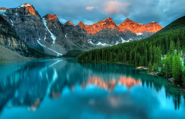 A stunning view of a tranquil lake surrounded by lush pine trees and snow-capped mountains during sunset, capturing the beauty of exploring Canada's scenic routes.