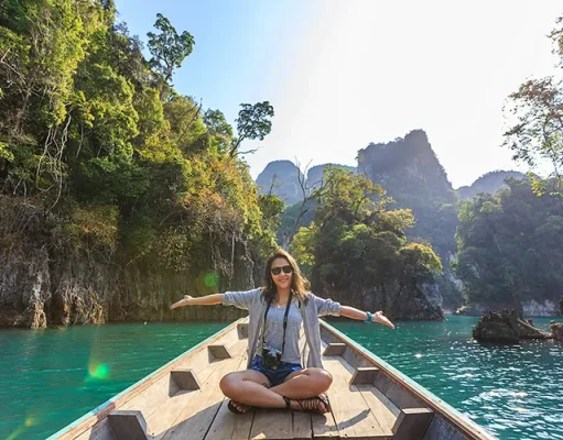 What People Do Online While Traveling the World A woman spreading her hands on a boat on a body of water, surrounded by hills and trees.