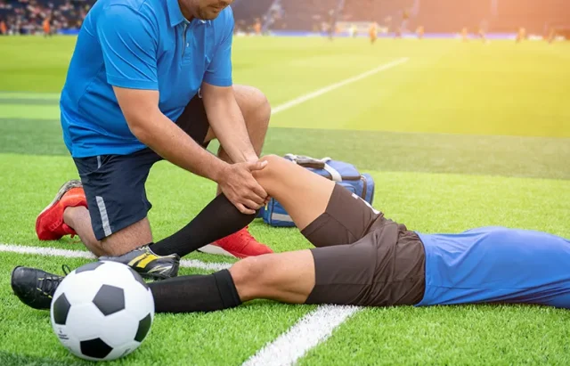 low-section-male-physical-therapist-rubbing-soccer-player-knee-field copy