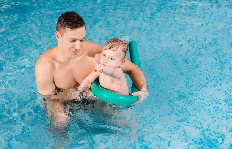 Certified swim instructor at Nemo Swim School gently supports a smiling toddler during a private water safety lesson in the pool.