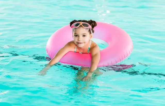 Private Swim Lessons-topaz-upscale-2x copy A young girl smiles during her swim lesson at Nemo Swim School, wearing a floatation ring and children’s swim goggles in the pool.