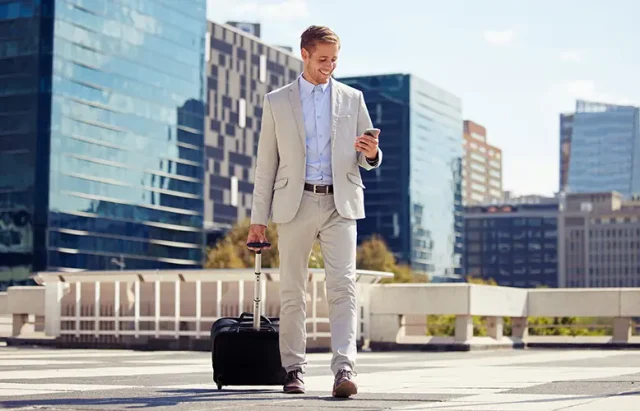 smile-phone-businessman-city-with-luggage-travel-commute-reading-email-outdoor-mobile-happy-professional-suitcase-street-journey-walking-salesman-online-news-app copy