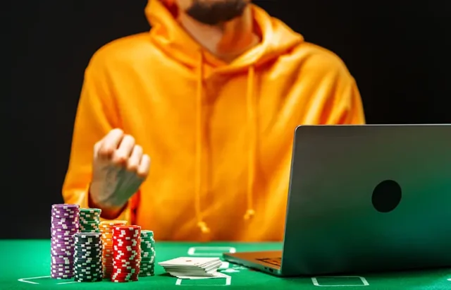 person-orange-hoodie-plays-online-poker-with-chips-cards-green-felt-table-while-focused-laptop-screen copy