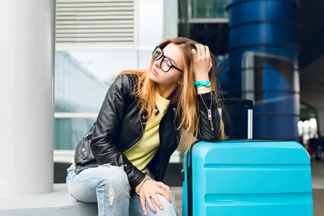 portrait-pretty-girl-with-long-hair-glasses-sitting-outside-airport-she-wears-yellow-sweater-with-black-jacket-jeans-she-leaned-suitcase-is-looking-far-away copy