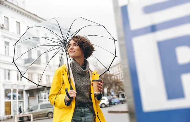 stylish-woman-yellow-raincoat-walking-through-urban-area-big-transparent-umbrella-holding-takeaway-coffee-hand copy