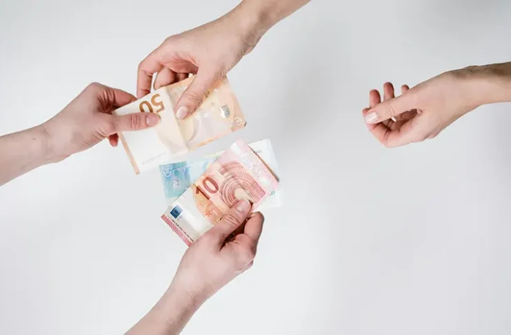 Overhead shot of three hands exchanging various Euro banknotes